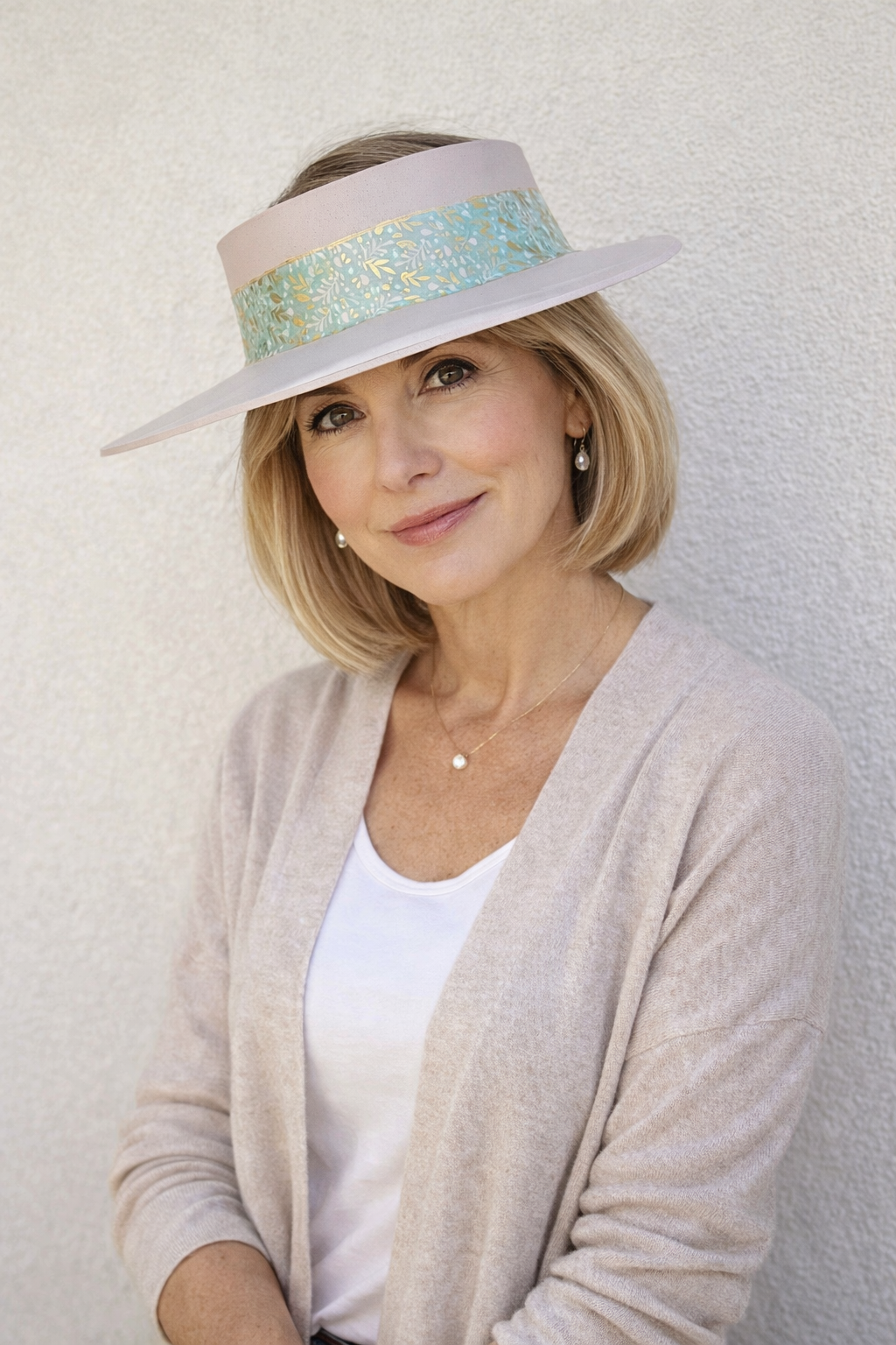 Woman wearing a light-colored visor with a decorative band against a plain background