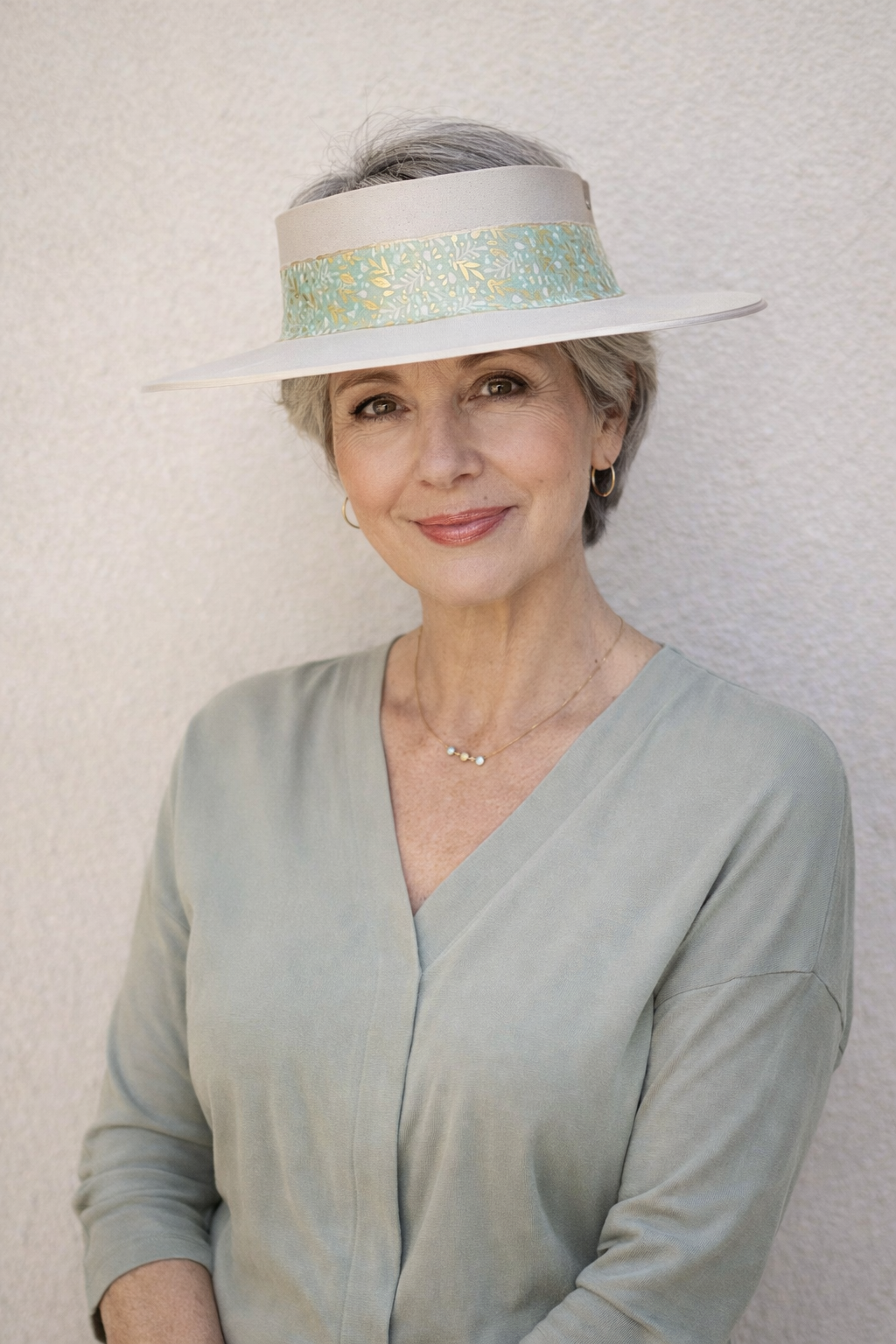 Woman wearing a light blue dress and a decorative visor against a plain background