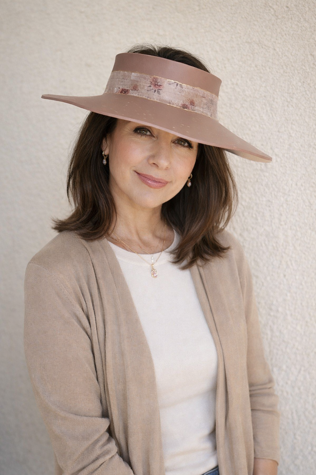 Woman wearing a wide-brimmed hat with a floral band against a plain background