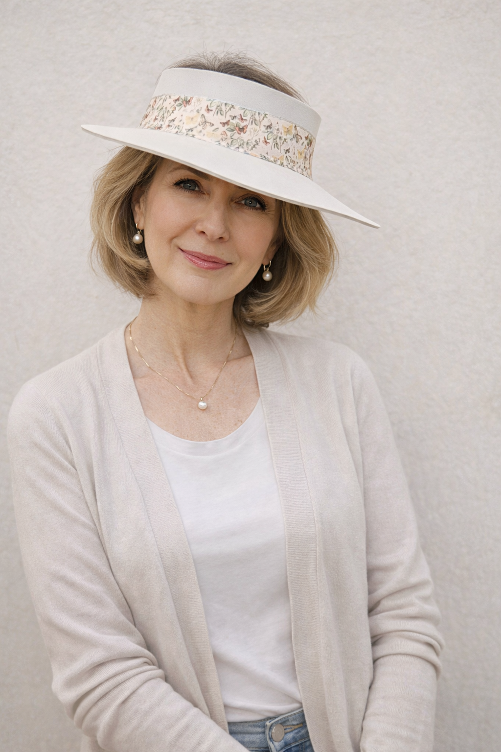 Woman wearing a white visor hat with decorative band on a plain background