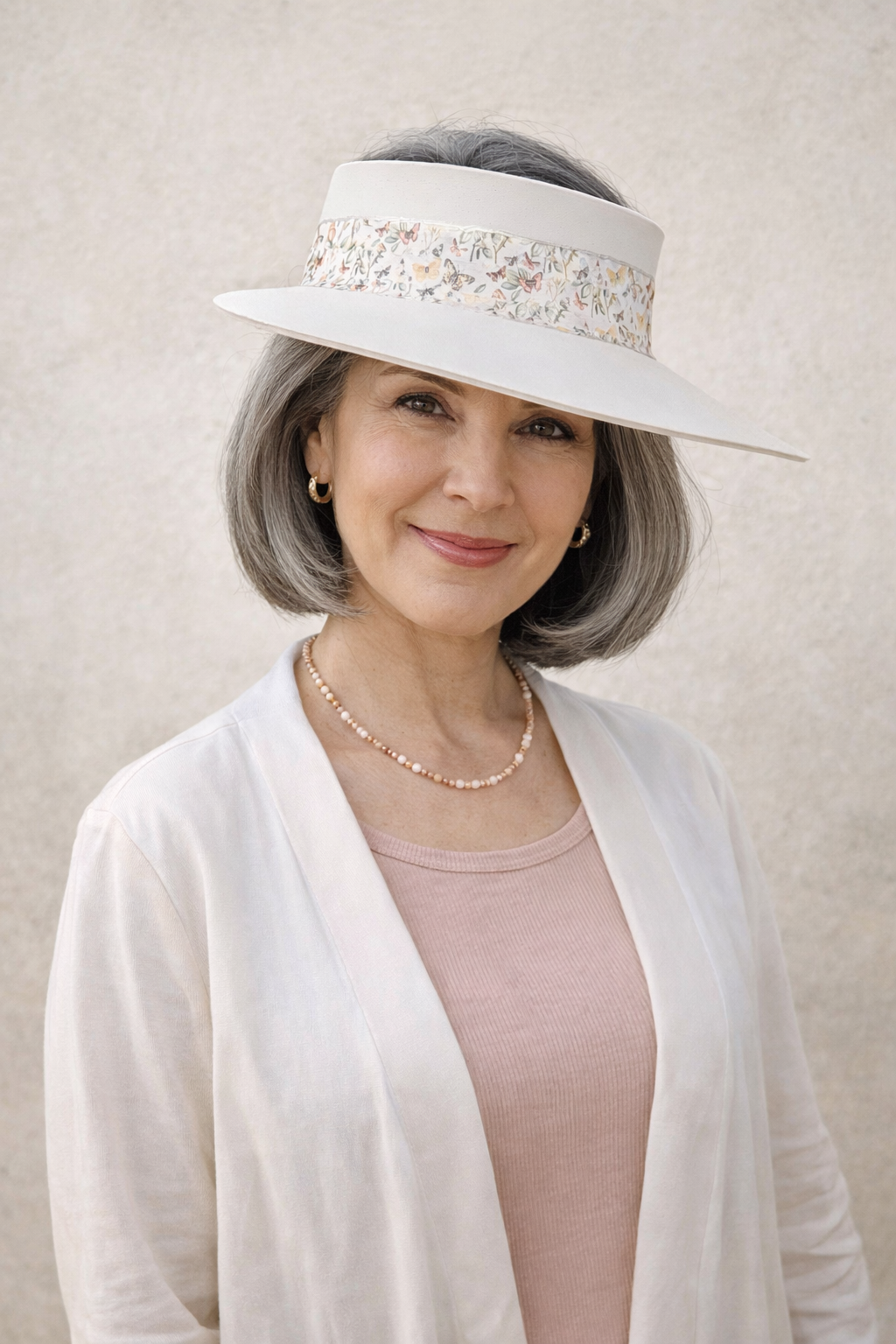 Woman wearing a white visor with decorative band and pearl necklace against a beige background