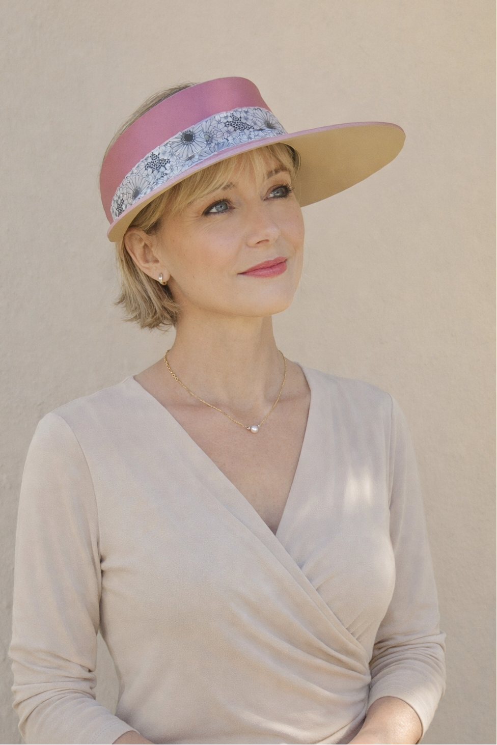 Woman wearing a beige visor with a pink band and floral pattern against a plain background
