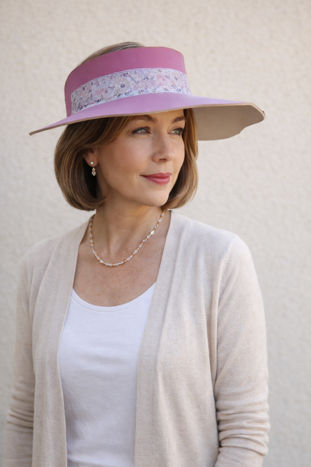 Woman wearing a pink visor with floral band against a beige background
