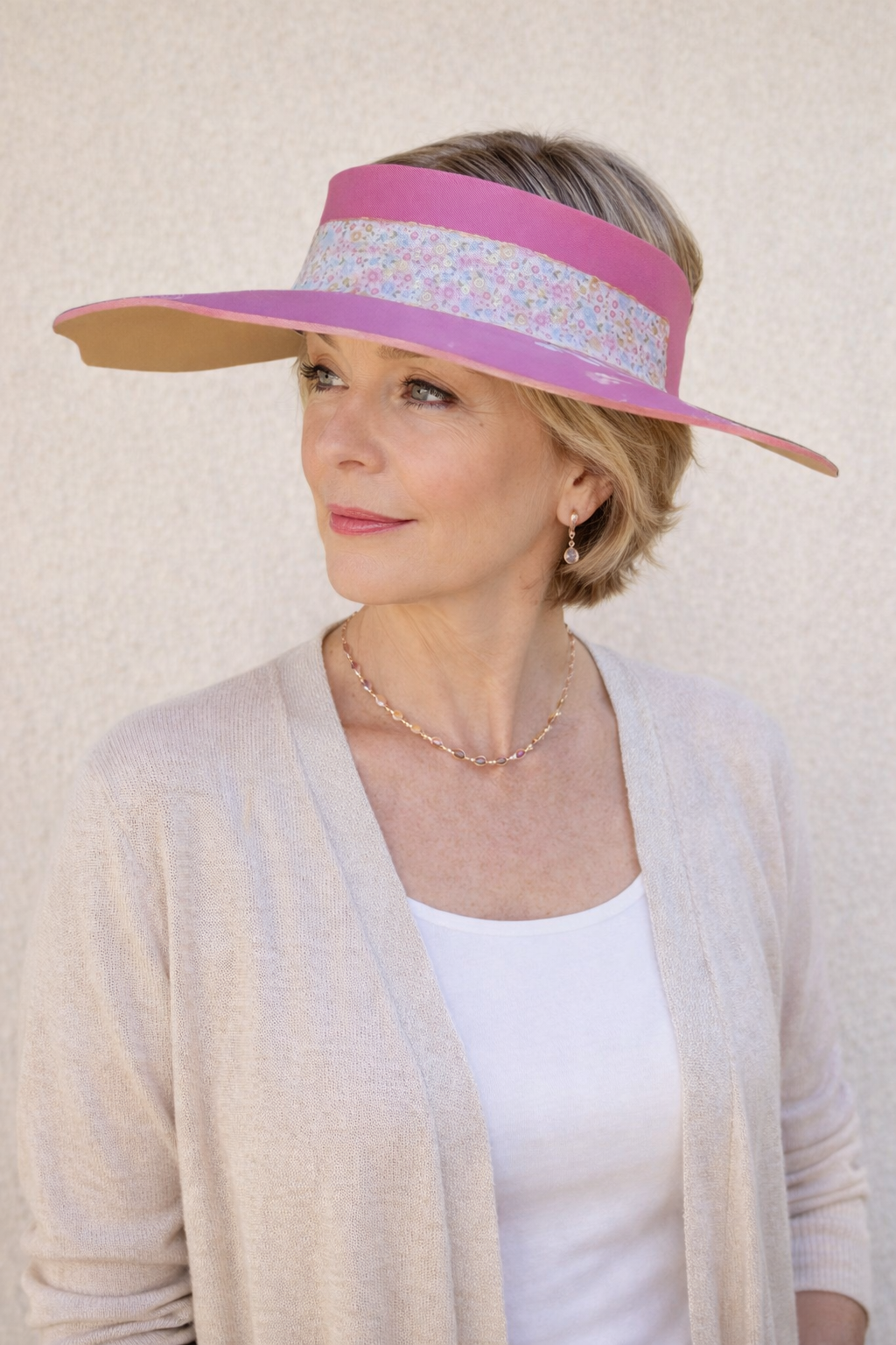 Woman wearing a wide-brimmed hat with a pink band against a plain background