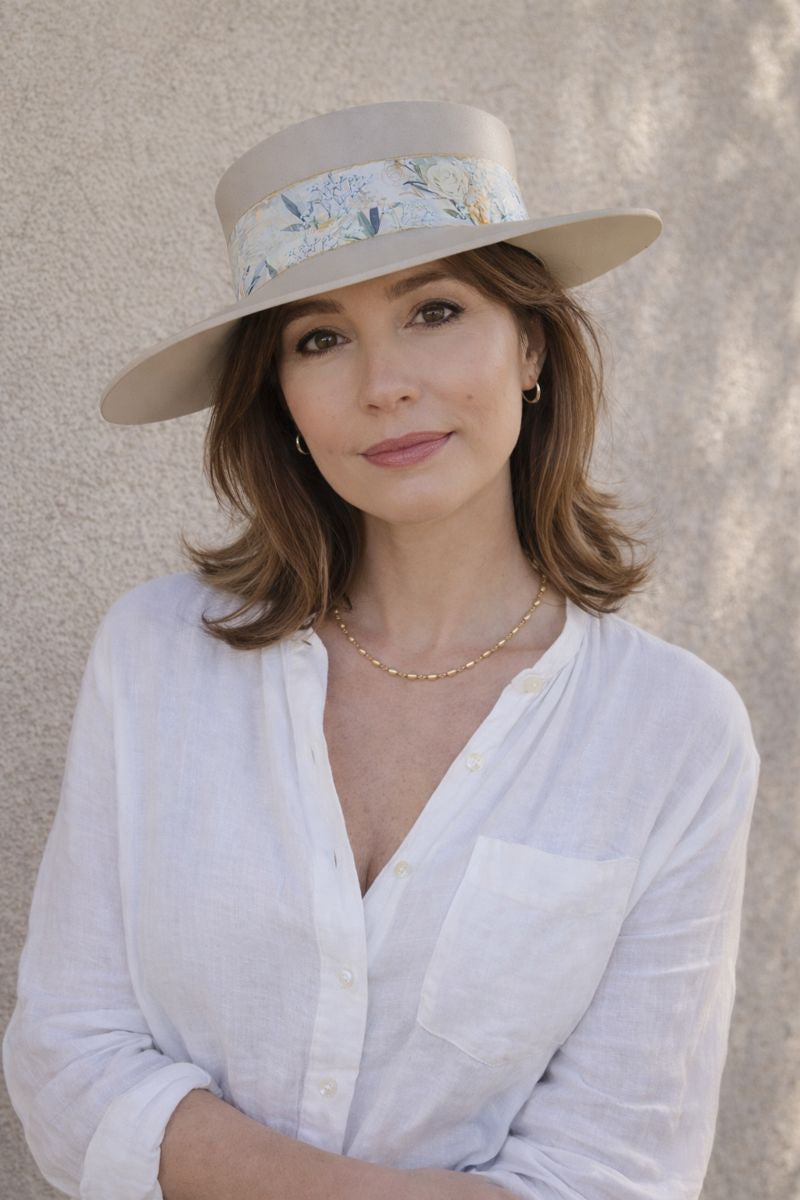 Woman wearing a beige hat with floral band and white shirt against a neutral background