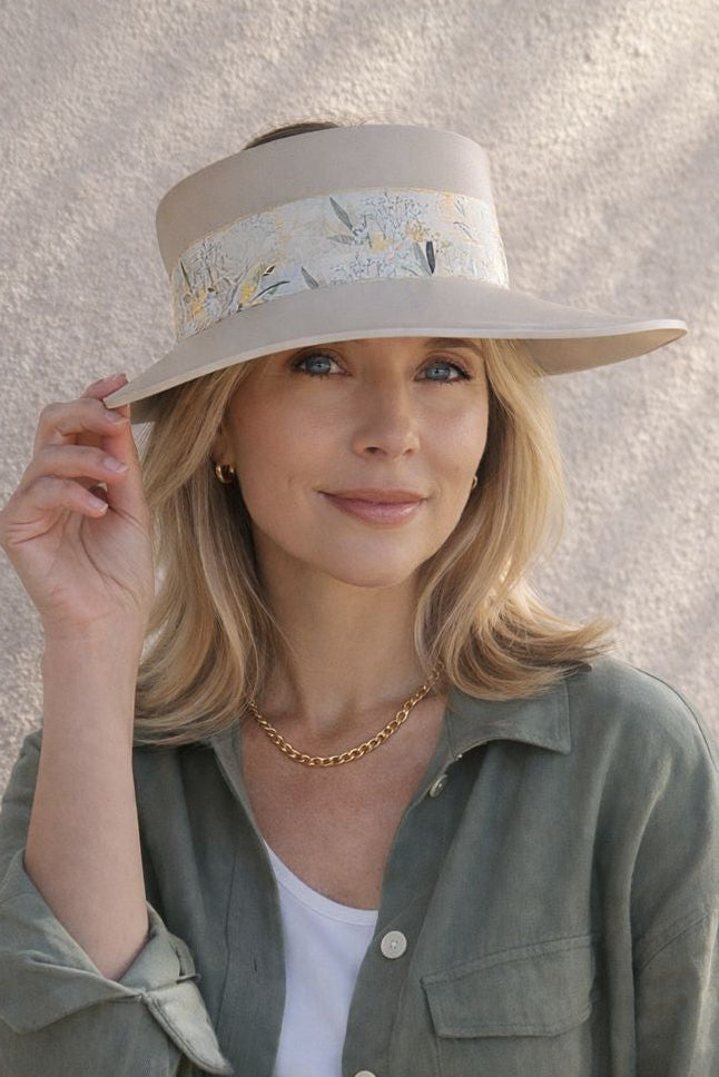 Woman wearing a wide-brimmed hat with a floral band against a textured wall.