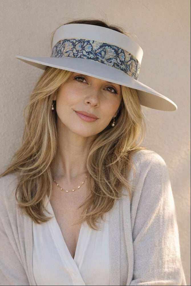 Woman wearing a wide-brimmed hat with floral band against a beige wall