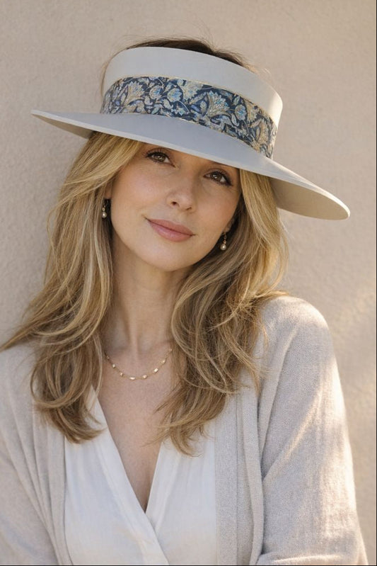 Woman wearing a wide-brimmed hat with floral band against a beige wall