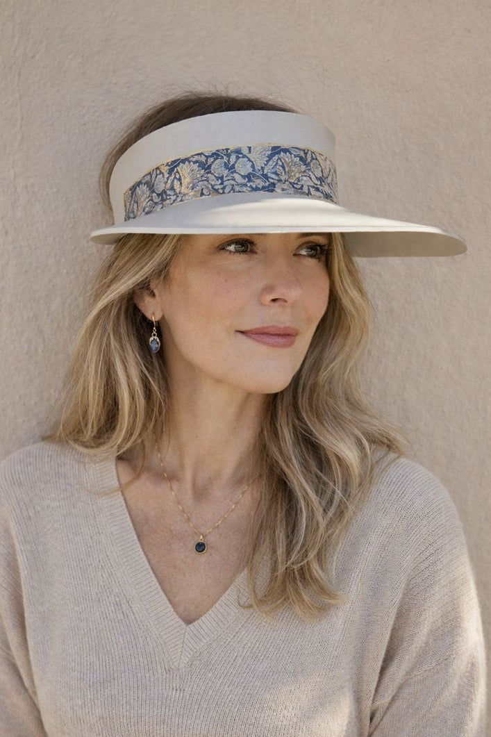 Woman wearing a wide-brimmed hat with floral band against a beige wall