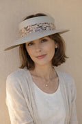 Woman wearing a wide-brimmed hat with floral band against a beige wall