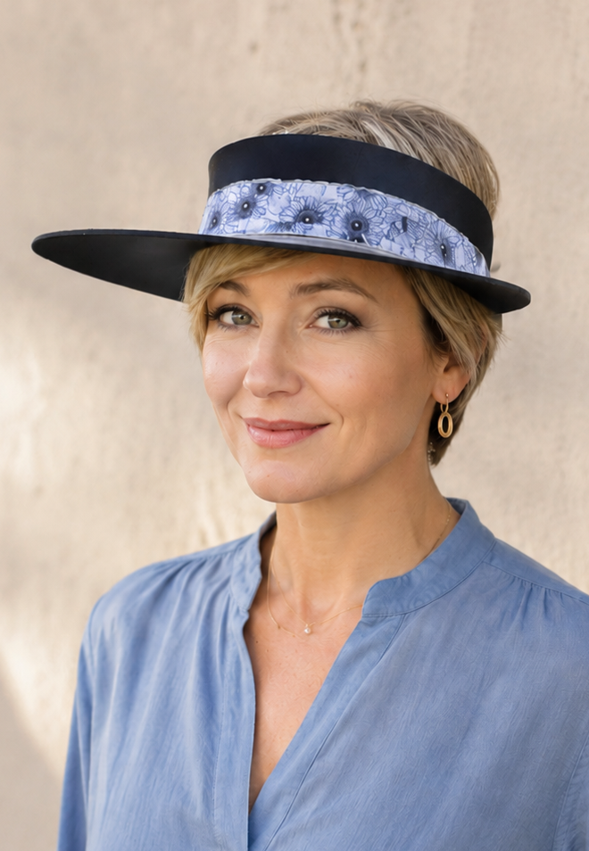 Woman wearing a blue shirt and a black hat with a decorative band against a neutral background