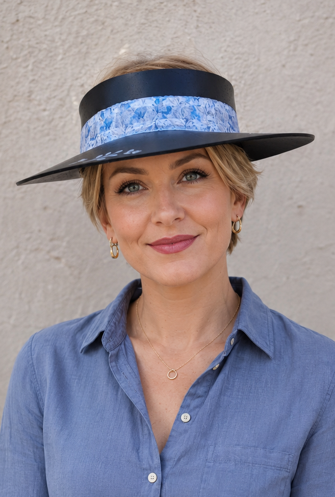 Woman wearing a blue shirt and a wide-brimmed hat with a decorative band against a plain background