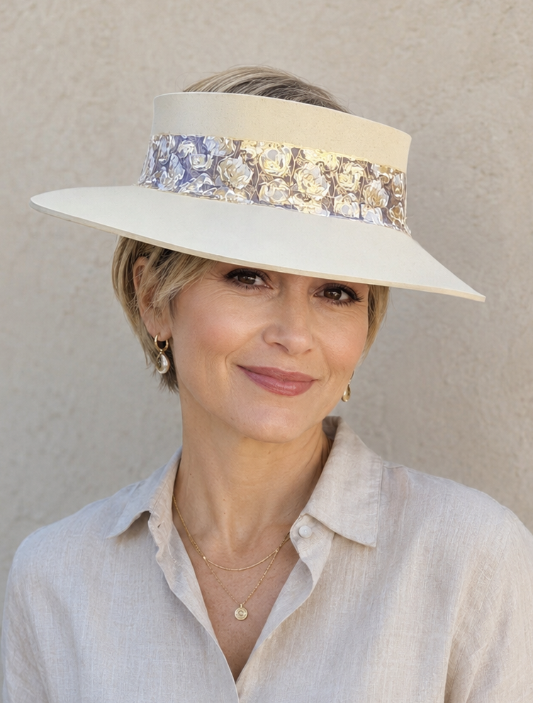 Woman wearing a wide-brimmed hat with floral embellishments against a plain background