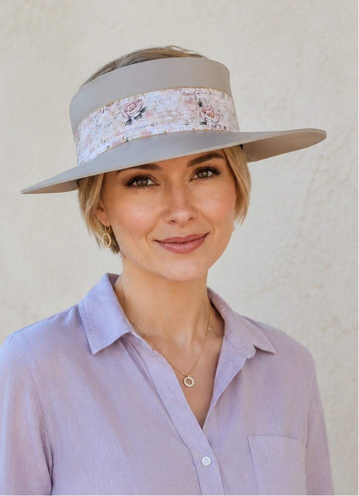 Woman wearing a light purple shirt and a wide-brimmed hat with a decorative band against a plain background
