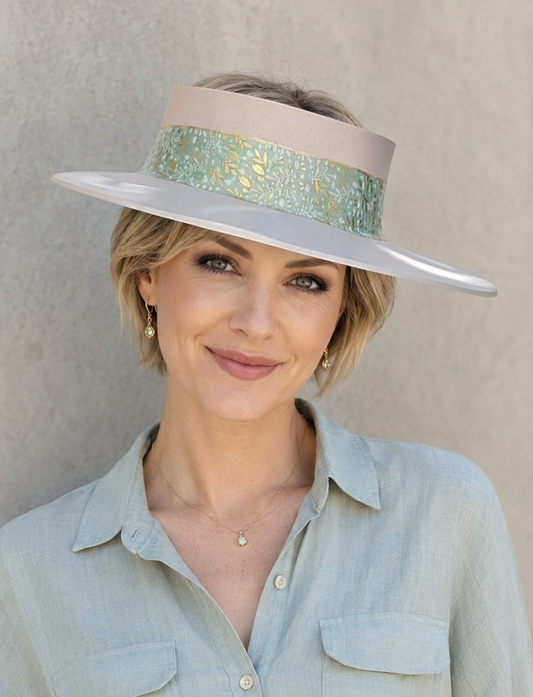 Woman wearing a light blue shirt and a wide-brimmed hat with a decorative band against a beige background