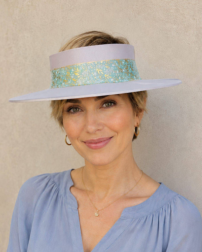 Woman wearing a light blue blouse and a sun visor hat with a decorative band against a beige background