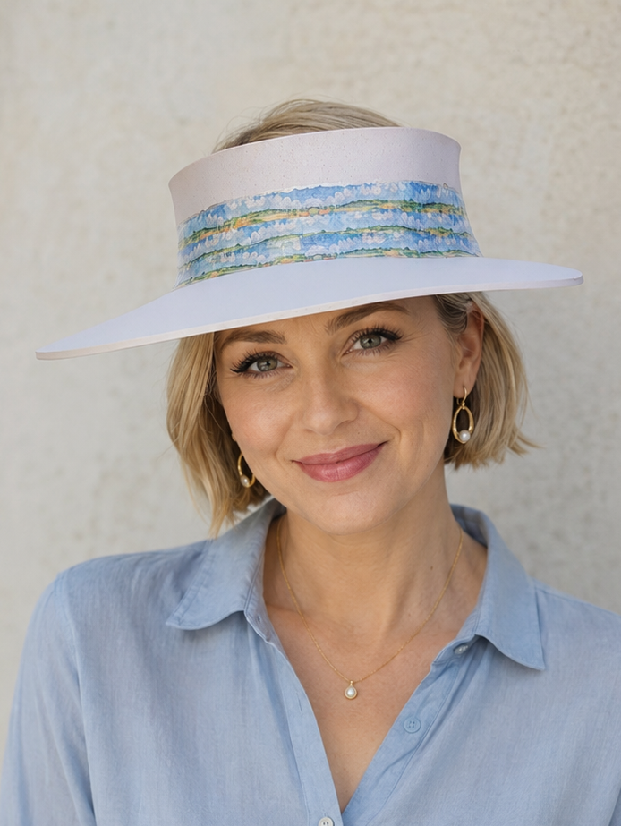 Woman wearing a light blue shirt and a wide-brimmed hat with decorative band against a neutral background