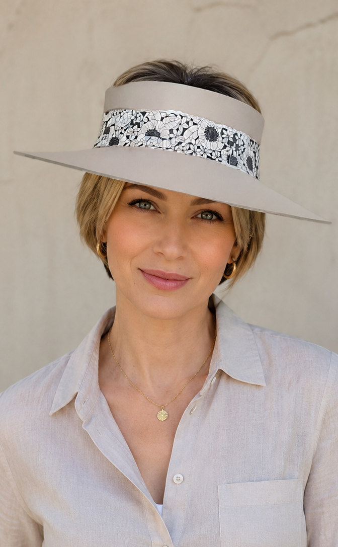 Woman wearing a beige visor with floral pattern, light-colored shirt, and white pants against a neutral background