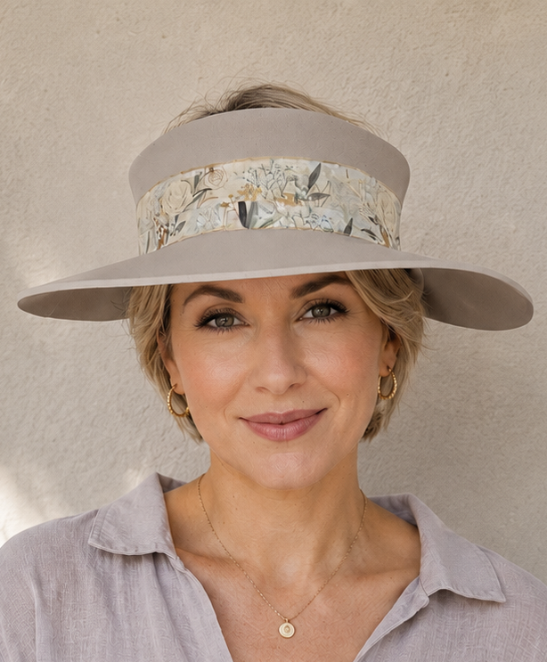 Woman wearing a light gray visor hat and shirt against a beige wall