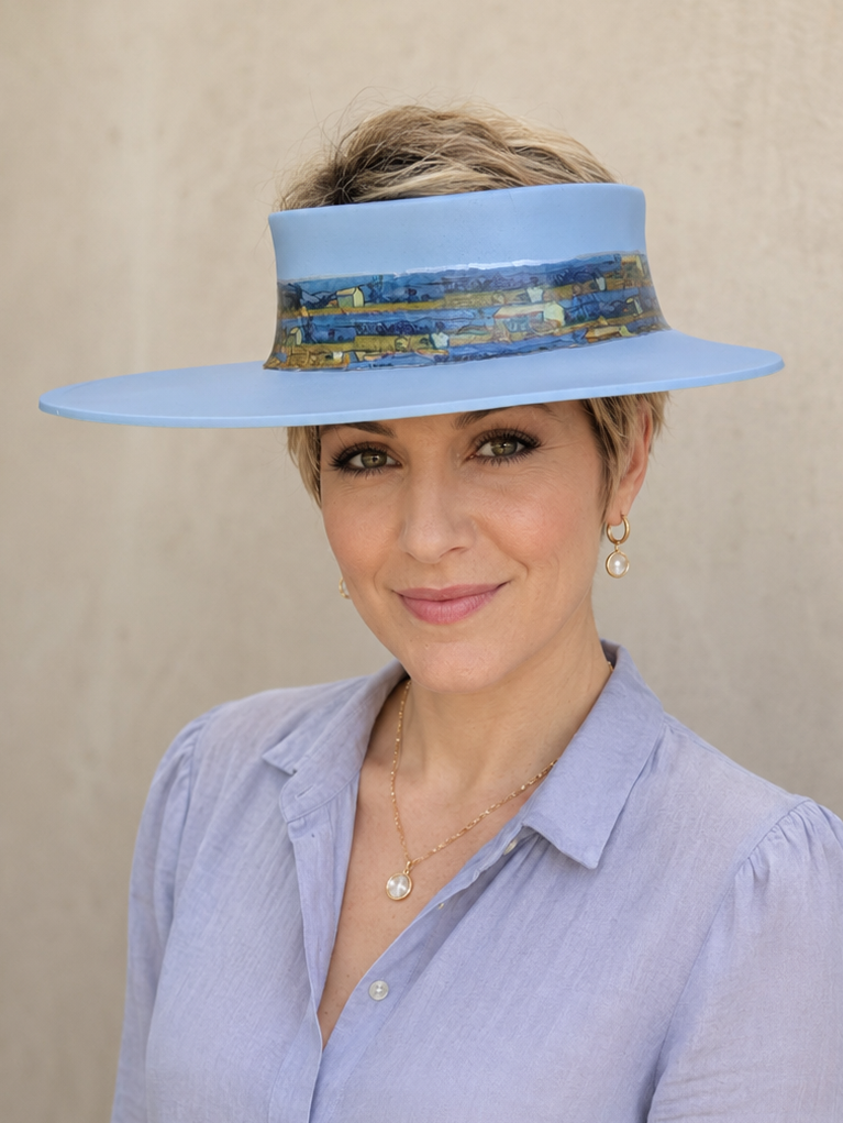 Woman wearing a wide-brimmed blue hat with a patterned band against a beige background