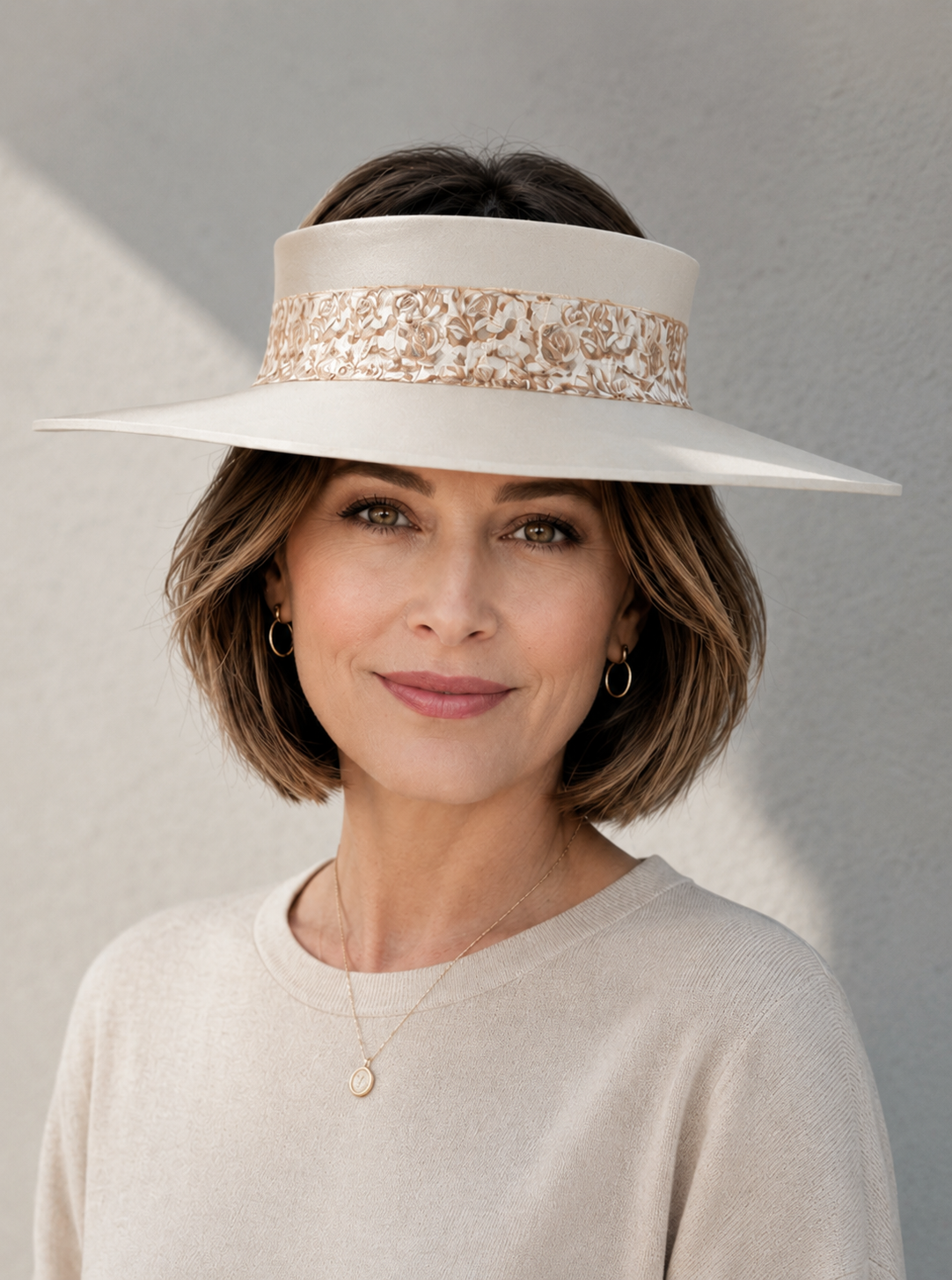 Woman wearing a white wide-brimmed hat with floral embellishments against a gray background