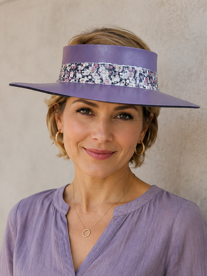 Woman wearing a purple hat with a floral band and matching blouse against a neutral wall.