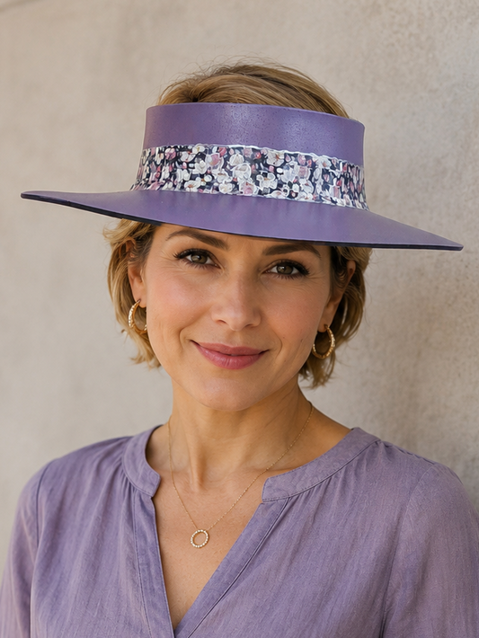 Woman wearing a purple hat with a floral band and matching blouse against a neutral wall.