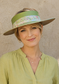 Woman wearing a green visor hat with floral band against a beige wall