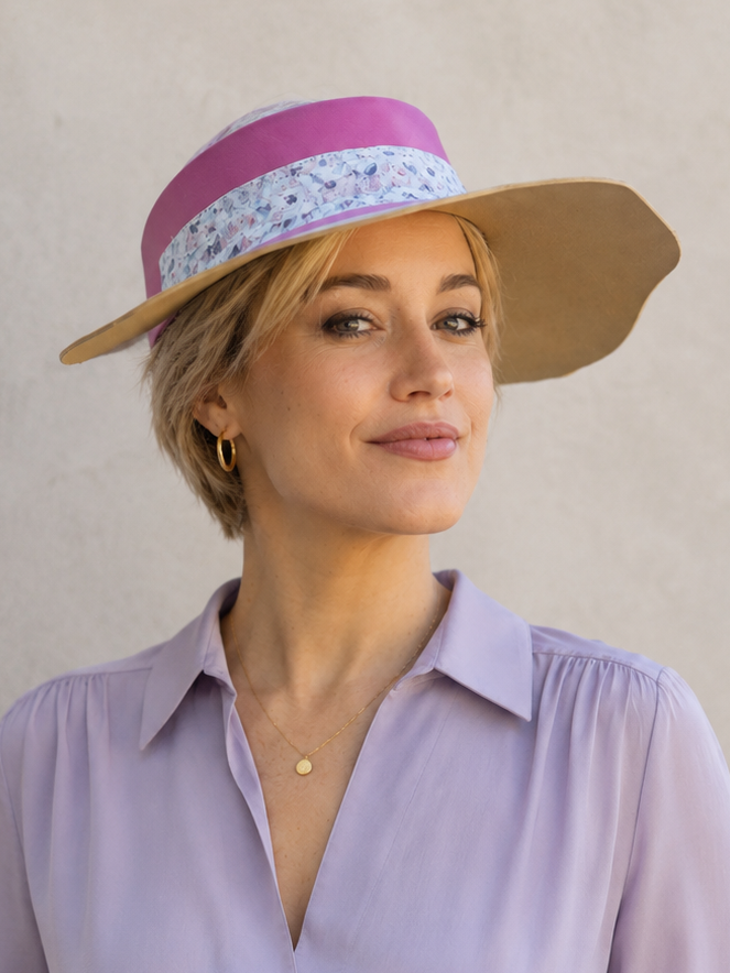 Woman wearing a light purple blouse and a wide-brimmed hat with a pink band against a neutral background