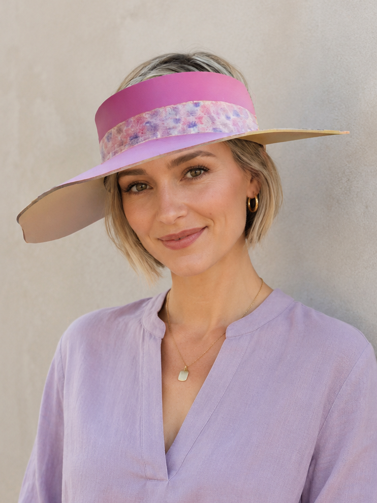 Woman wearing a light purple blouse and a wide-brimmed hat with a floral band against a neutral background