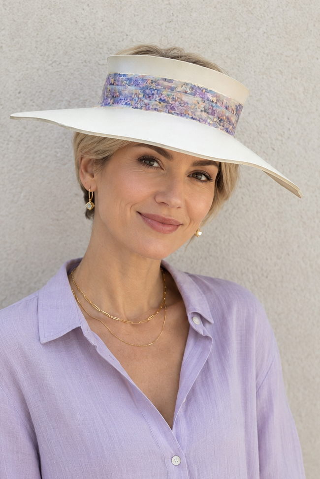 Woman wearing a light purple shirt and a white visor with floral band against a plain background