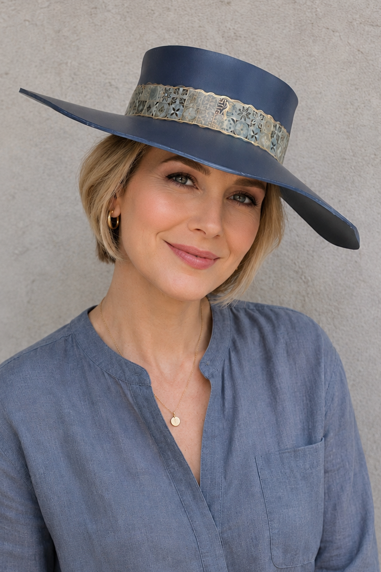 Woman wearing a wide-brimmed blue hat with a decorative band against a plain background