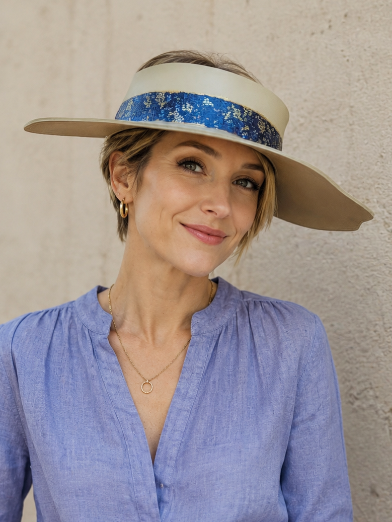 Woman wearing a blue shirt and beige visor with a floral band against a neutral background
