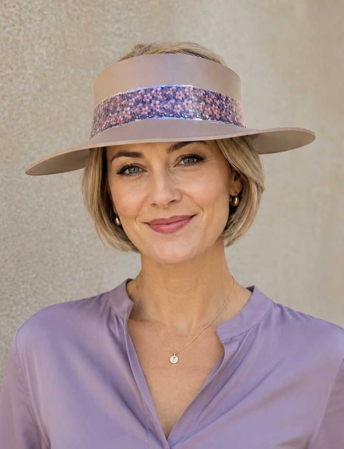 Woman wearing a light purple blouse and a beige hat with a floral band against a plain background