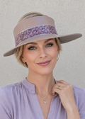 Woman wearing a light purple blouse and a wide-brimmed hat with a floral band against a plain background