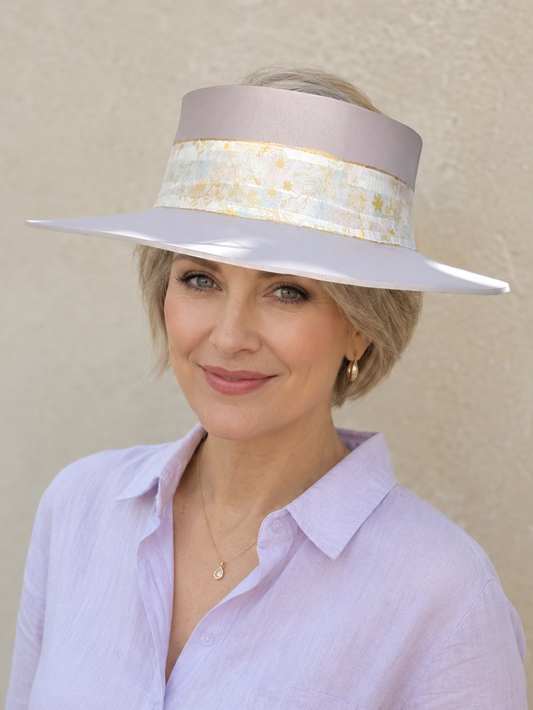 Woman wearing a light purple shirt and a wide-brimmed hat with a decorative band against a beige background