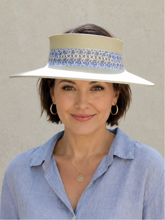 Woman wearing a light blue shirt and a white visor with decorative band against a plain background