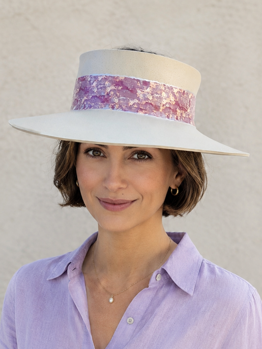Woman wearing a white hat with a colorful band and a light purple shirt against a beige background