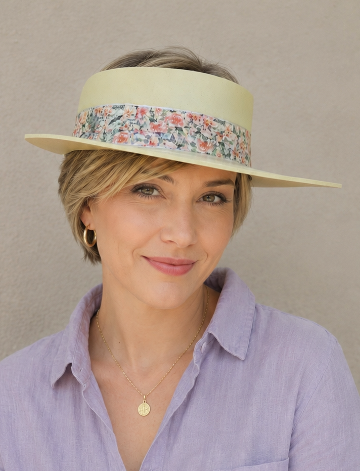 Woman wearing a wide-brimmed hat with a floral band against a plain background