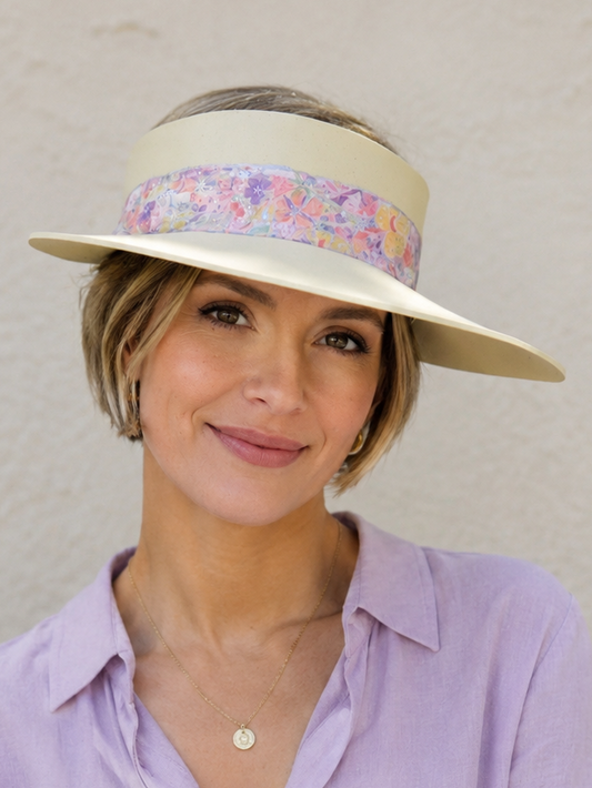Woman wearing a light purple shirt and a wide-brimmed hat with a colorful band against a plain background
