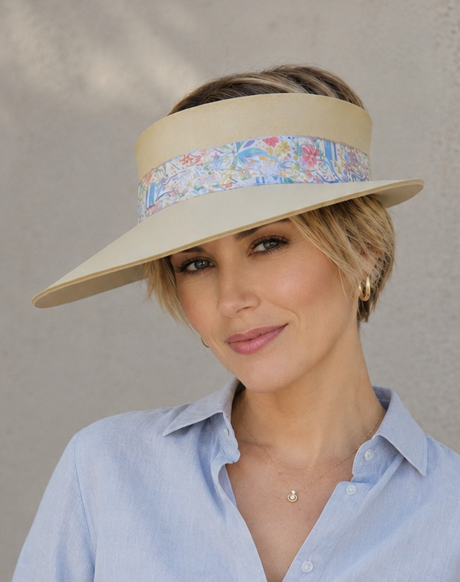 Woman wearing a light blue shirt and a wide-brimmed hat with a floral band against a neutral background