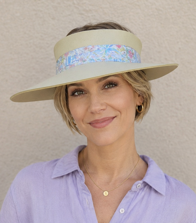 Woman wearing a light purple shirt and a wide-brimmed hat with floral band against a beige background