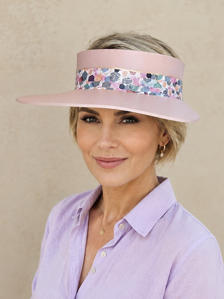 Woman wearing a light purple visor with floral pattern and matching shirt against a beige background