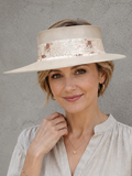 Woman wearing a wide-brimmed hat and beige shirt against a gray background