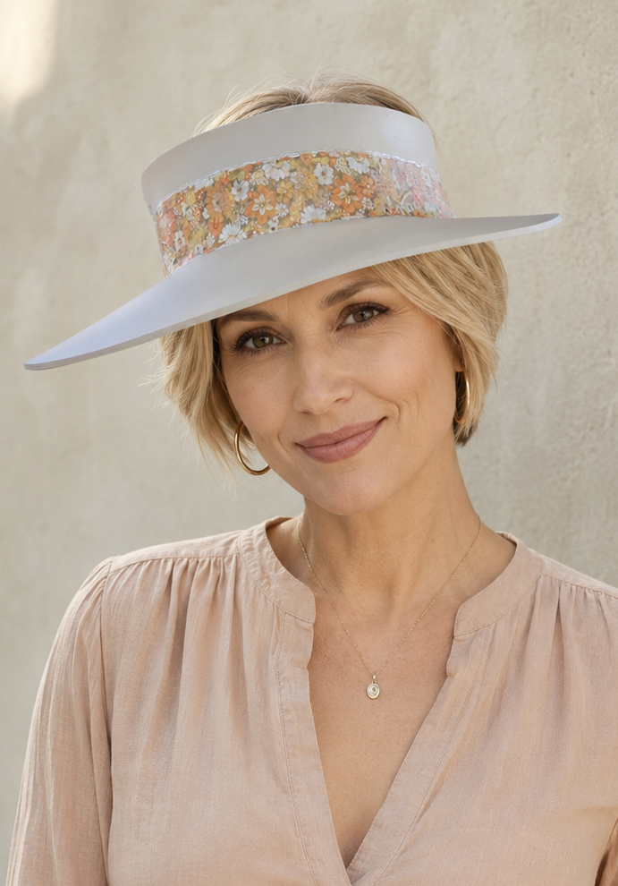 Woman wearing a wide-brimmed hat with a floral band against a neutral background