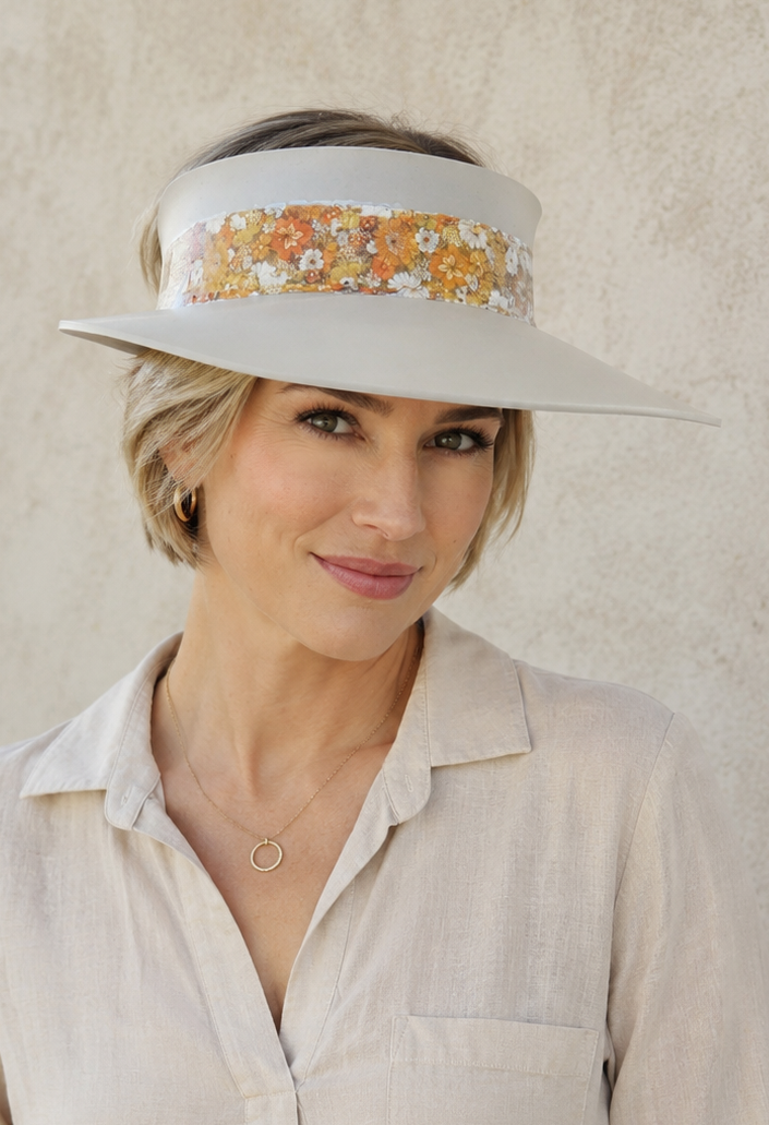 Woman wearing a light-colored shirt and floral visor against a plain background