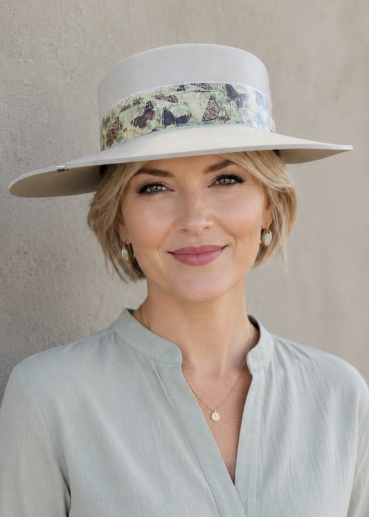 Woman wearing a light gray hat with floral band and matching shirt against a beige background