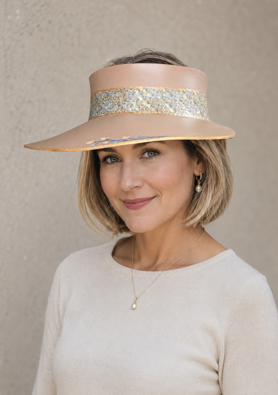 Woman wearing a beige hat with a decorative band against a neutral background