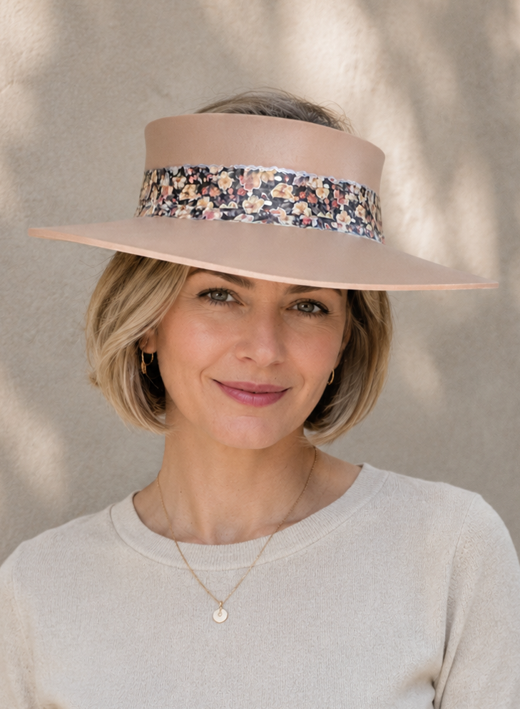 Woman wearing a beige visor hat with a floral band against a neutral background