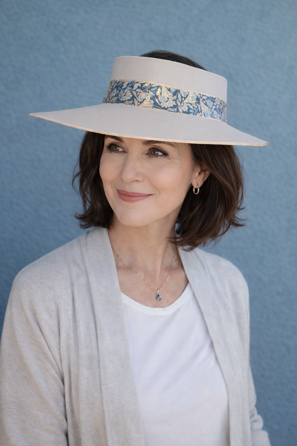 Woman wearing a wide-brimmed hat with floral band against a blue background